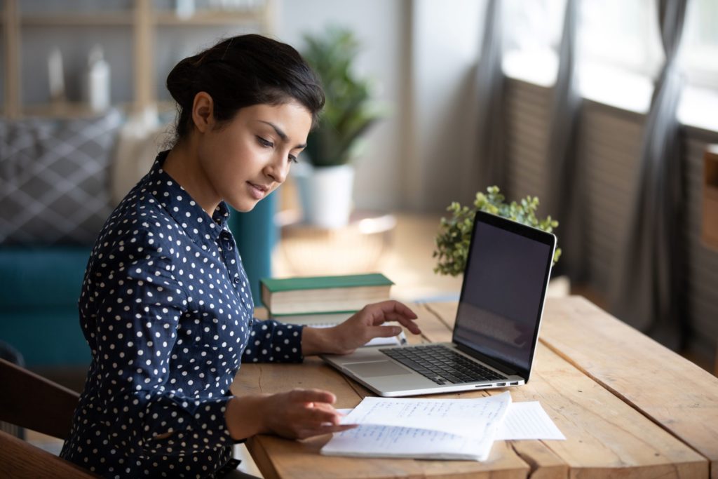A professional, young woman sits at her laptop, looking at her notes.
