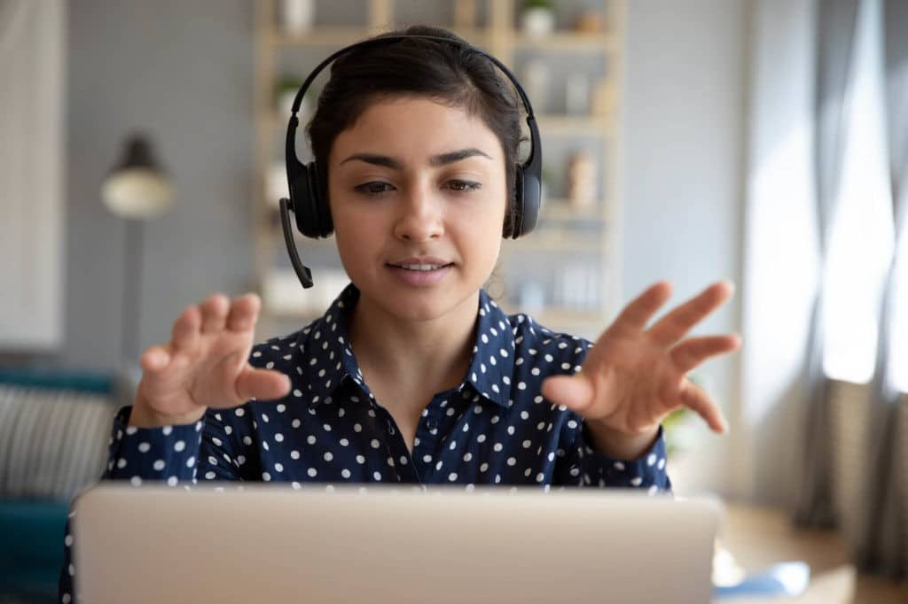 Young woman wearing headphones sitting in front of a laptop moving her hands.