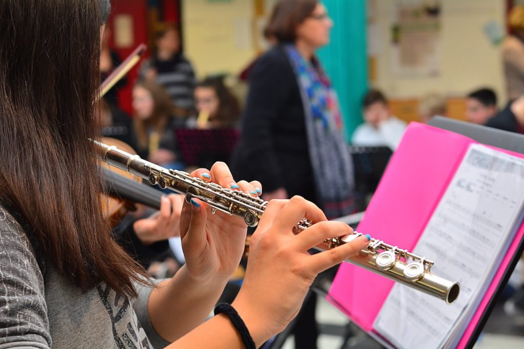 Female student playing the flute and reading music in a music classroom.