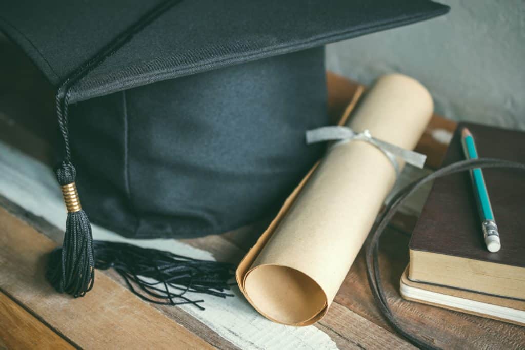 Graduation cap sitting next to a rolled up degree and books.