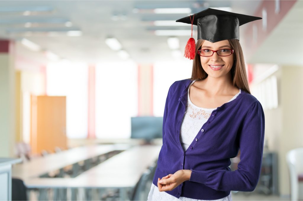 Woman teacher in a classroom wearing a graduation cap.