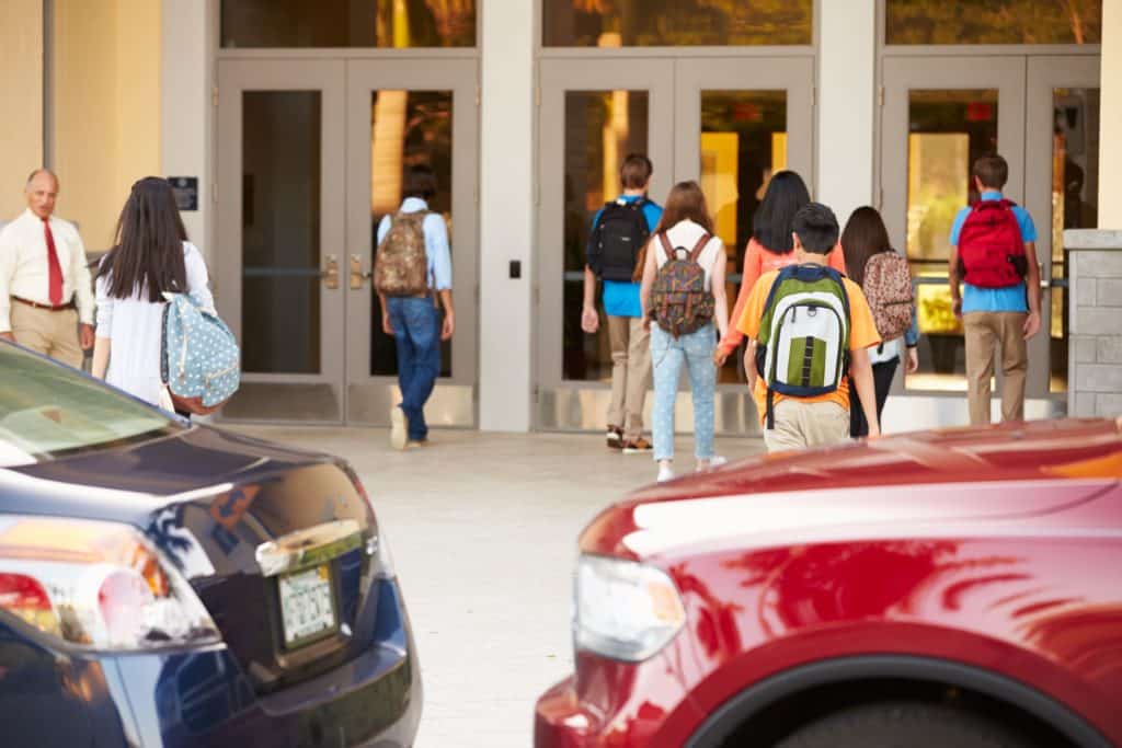 An administrator stands outside of the school doors as students get dropped off by parents.