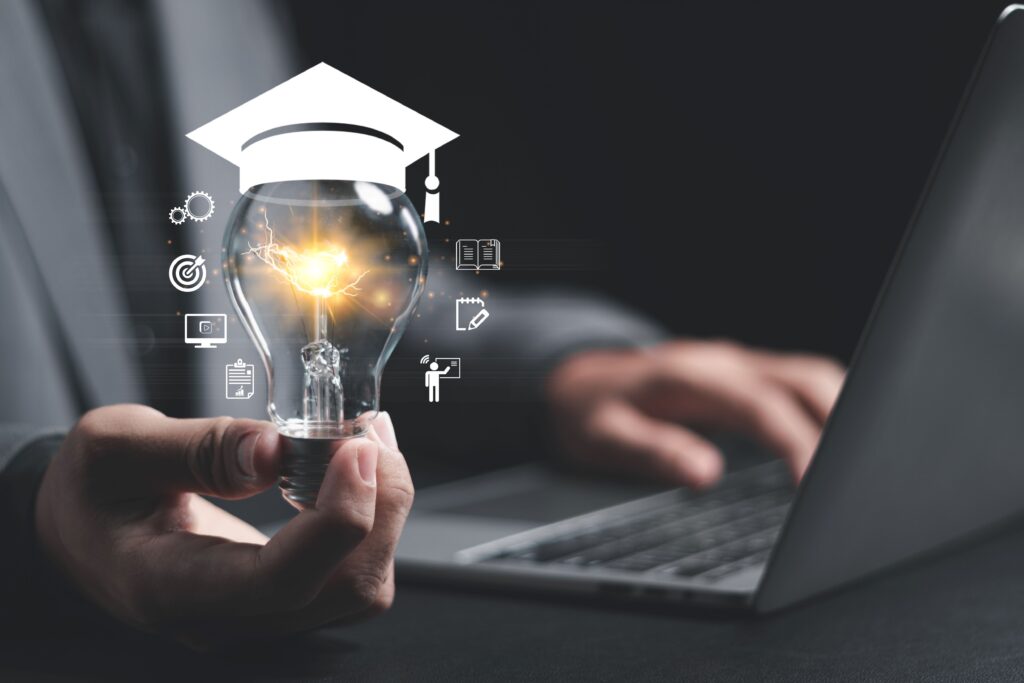 A person holds a light bulb that has a graduation cap sitting on top of it.