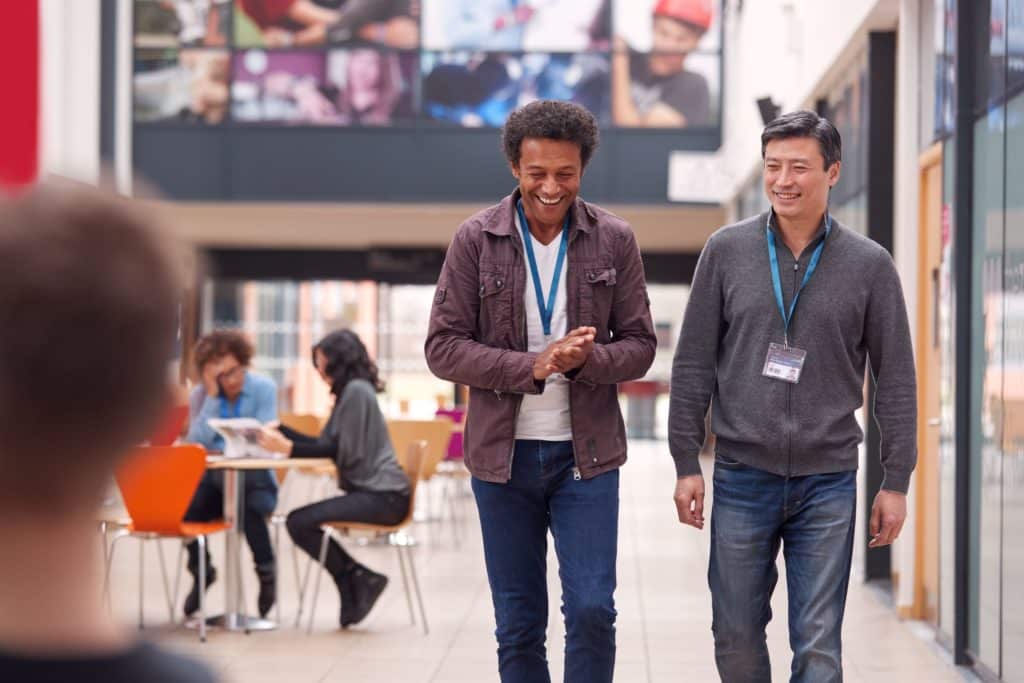 Two school professionals walk through the lunch room, smiling and talking.