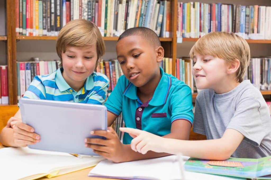 Young boys using a tablet together while in a library.
