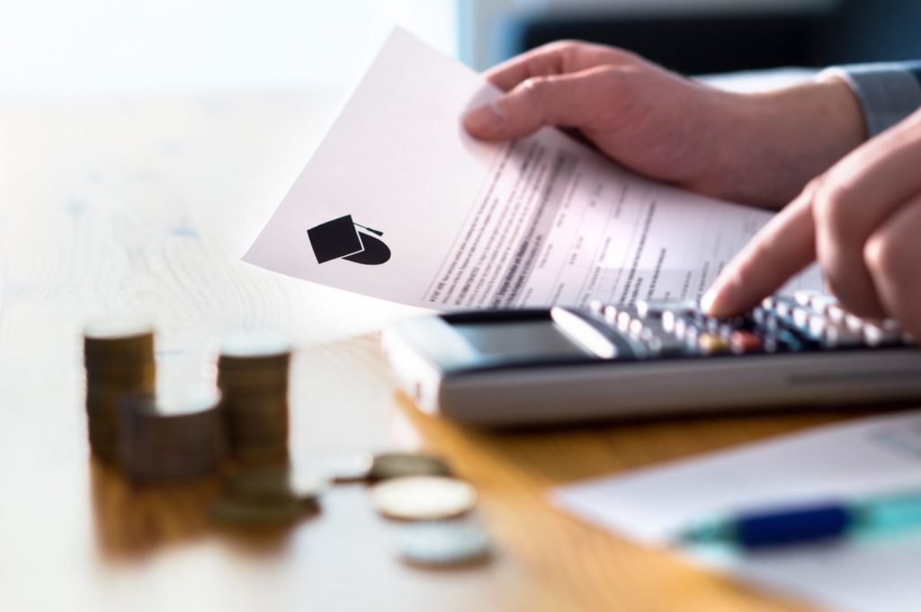 Man holding financial aid paperwork and using a calculator at a table with coins.