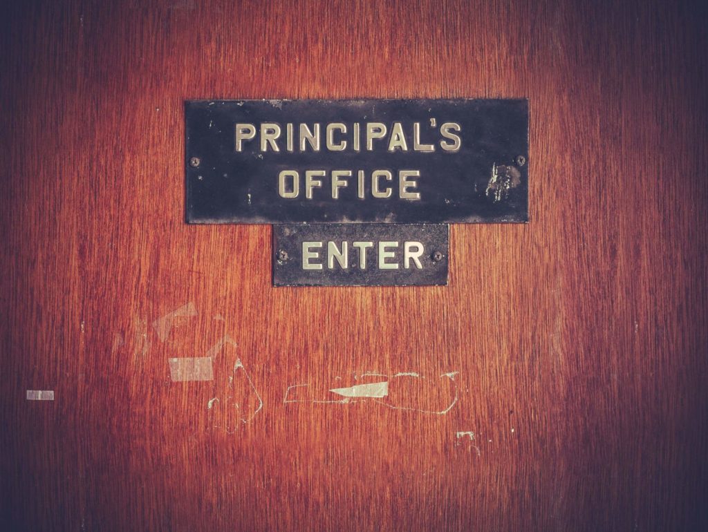 A school’s principal’s door with a plaque that reads “principal’s office: enter.”