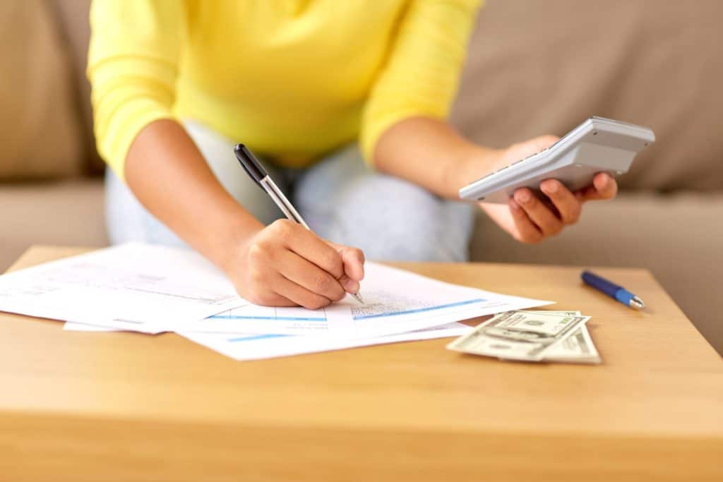 A woman calculates her finances at home with papers, a pen, and calculator around her.