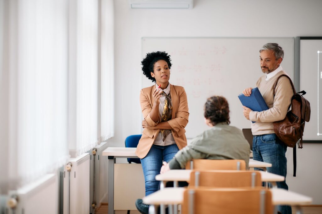 A group of three adults have a conversation in a classroom.