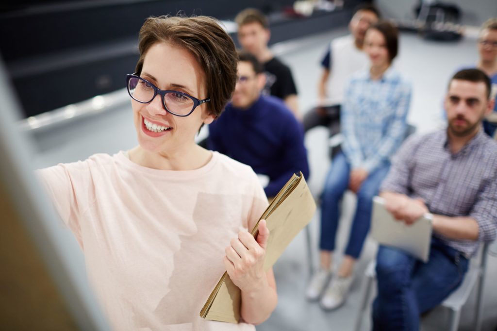 Woman holding a notepad writing on a white board in front of a group of adults.