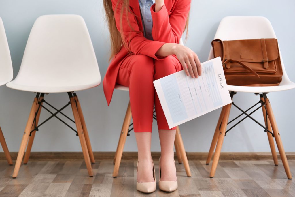A female professional sits waiting for a job interview, holding her resume paperwork.