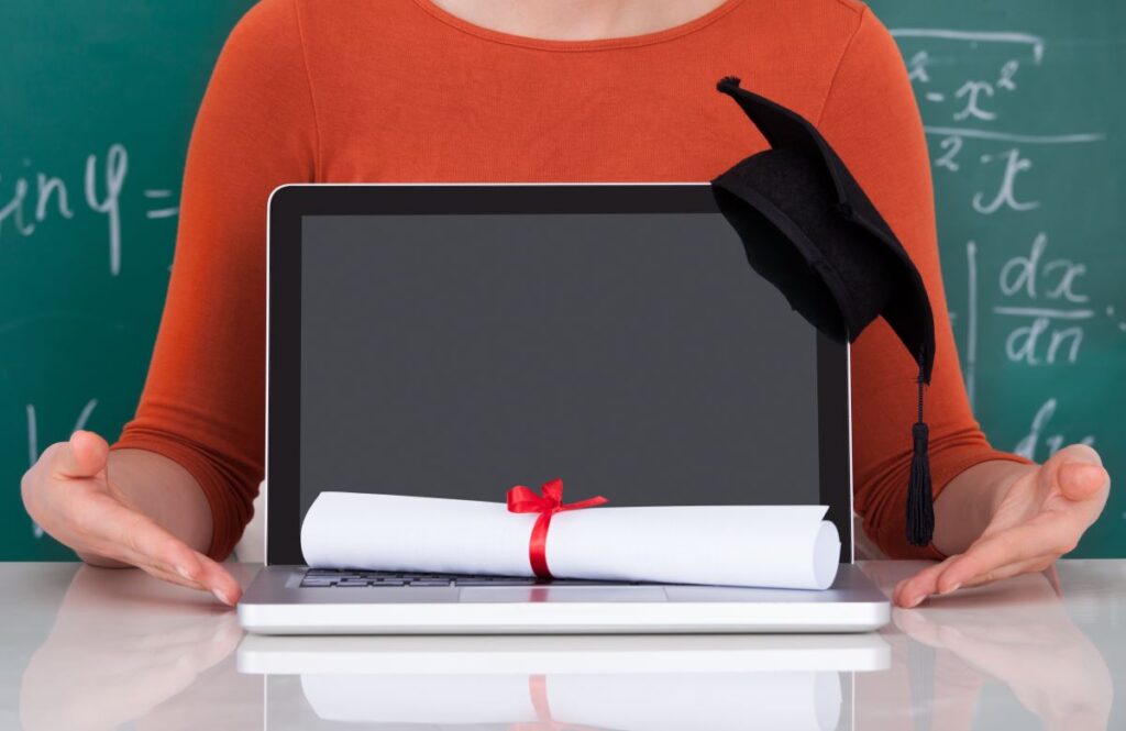 A close up of a laptop with a diploma and graduate cap sitting on it representing online degrees.