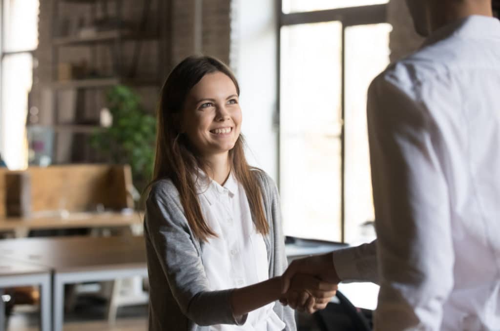 Young woman smiling and shaking hands with a man.