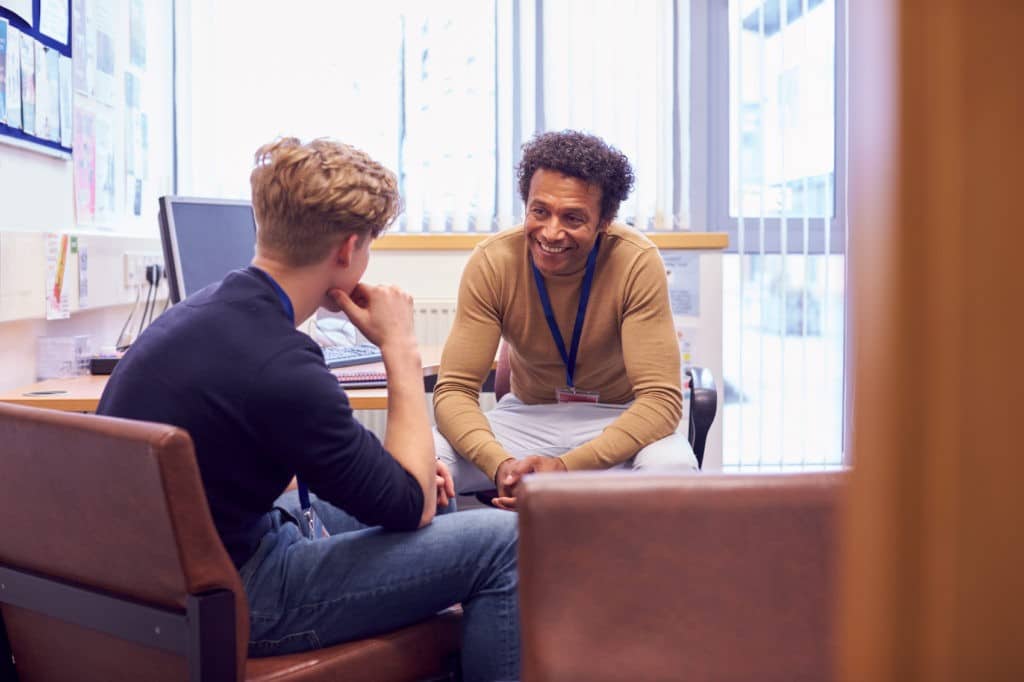 School counselor smiling and sitting with a student in his office.