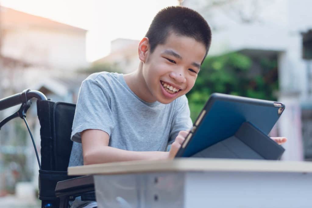 Young boy with special needs smiling and using a tablet.
