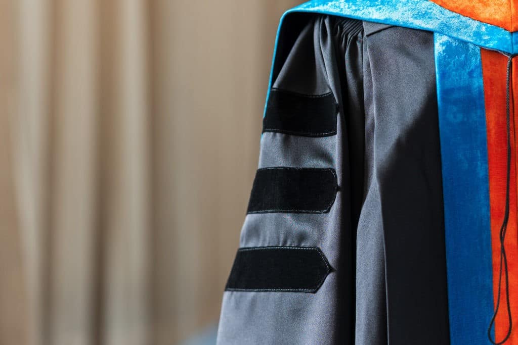 Doctoral graduate gown in front of a large curtain.
