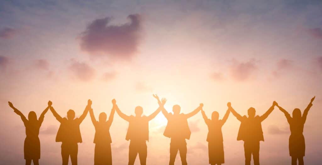 A group of workers stand together, holding their hands outstretched toward the sky in celebration.