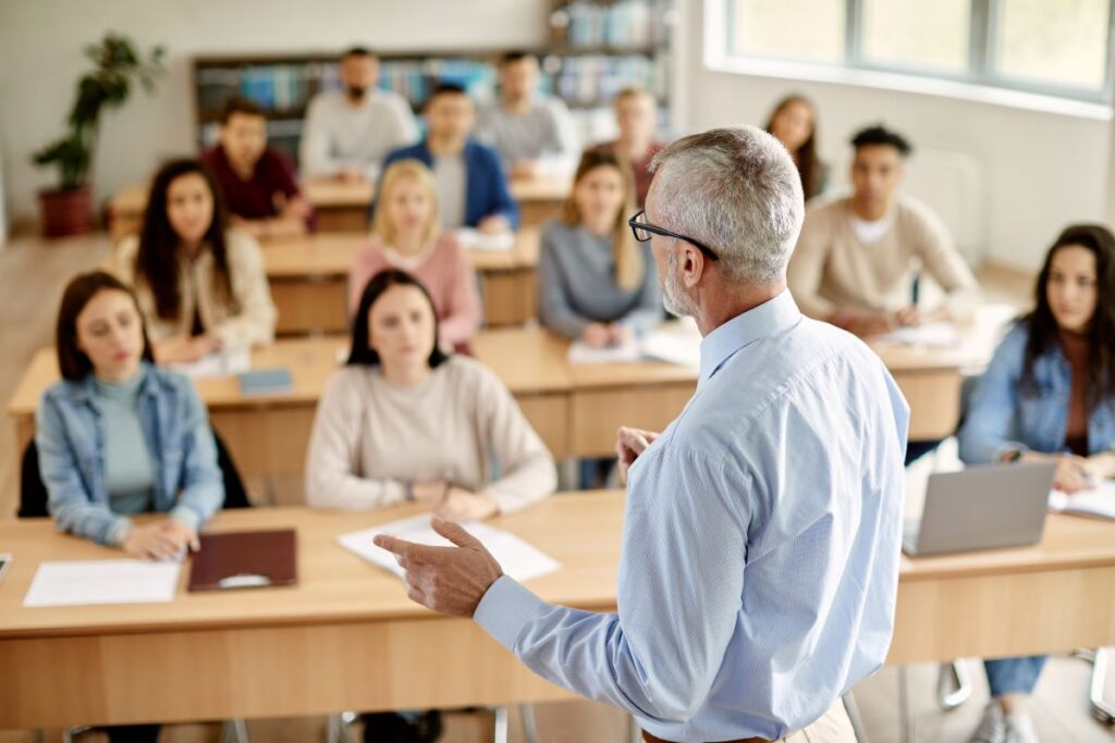 A higher education professor stands at the front of the class, leading a lecture.