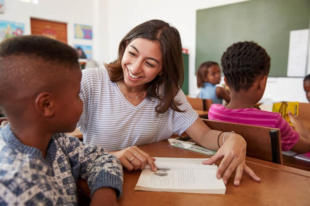 Young student teacher helping a young student at his desk.