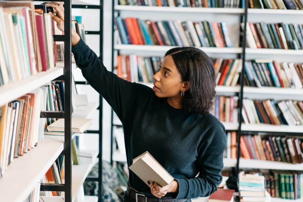 Young, female librarian sorts books on a bookshelf in a library.