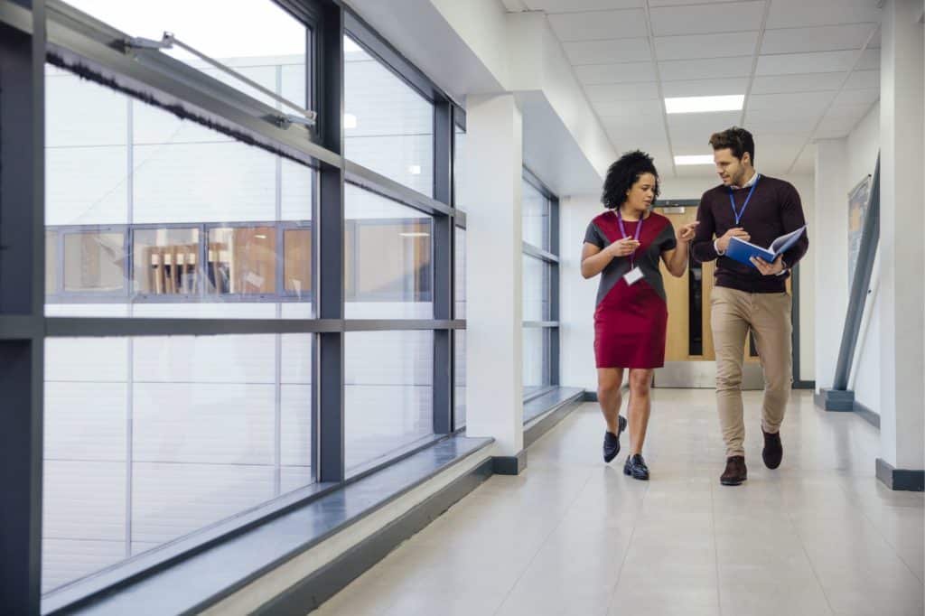 Two teachers walking down a hallway talking to each other.