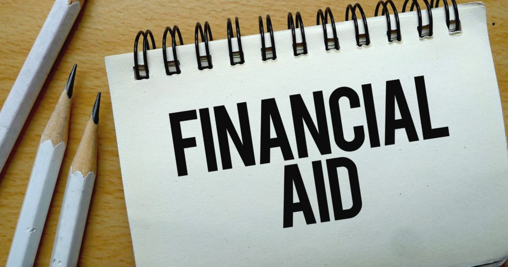 Notebook with the text financial aid on it, next to several pencils.