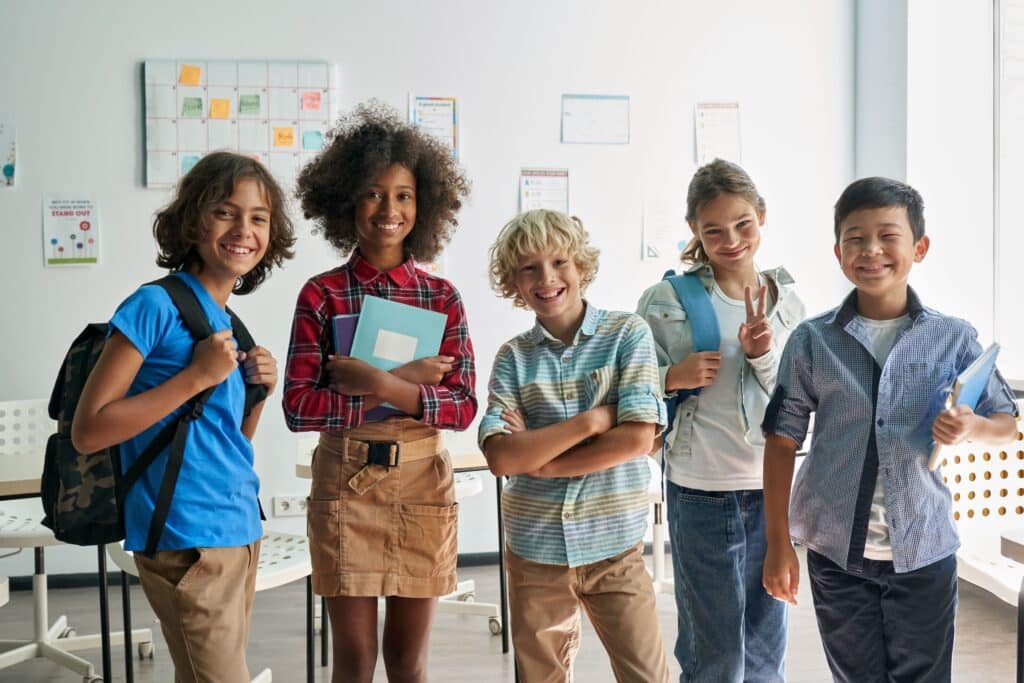 A group of diverse students stand together in the classroom smiling.