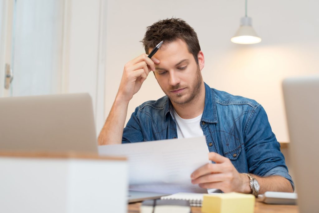 Young man sitting at a table studying a piece of paper.