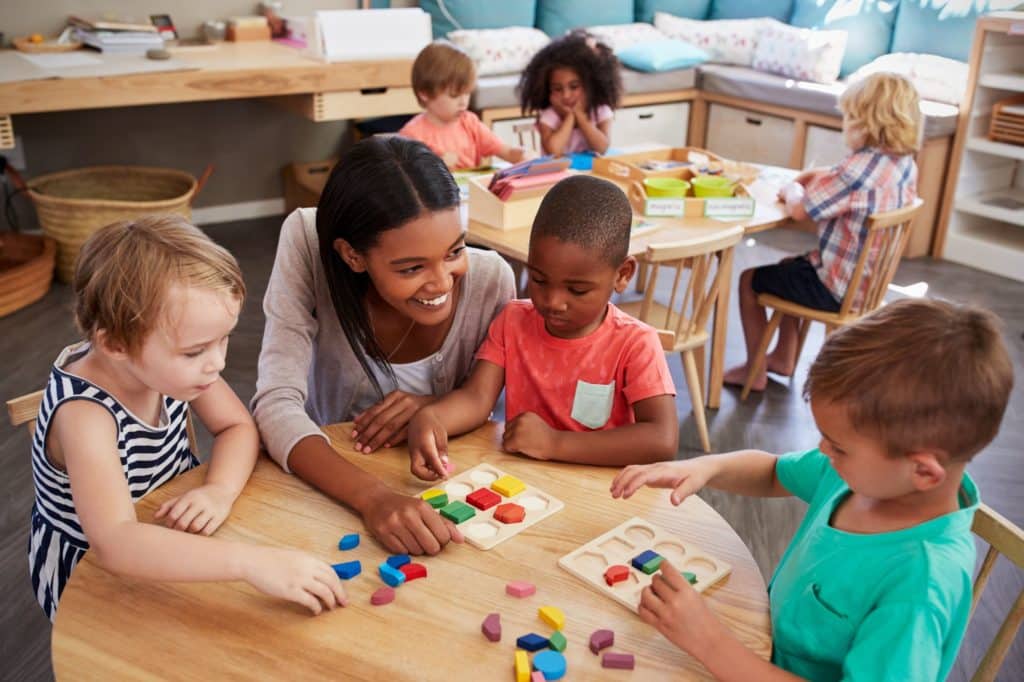 Young teacher smiling and helping a group of young students at a table.