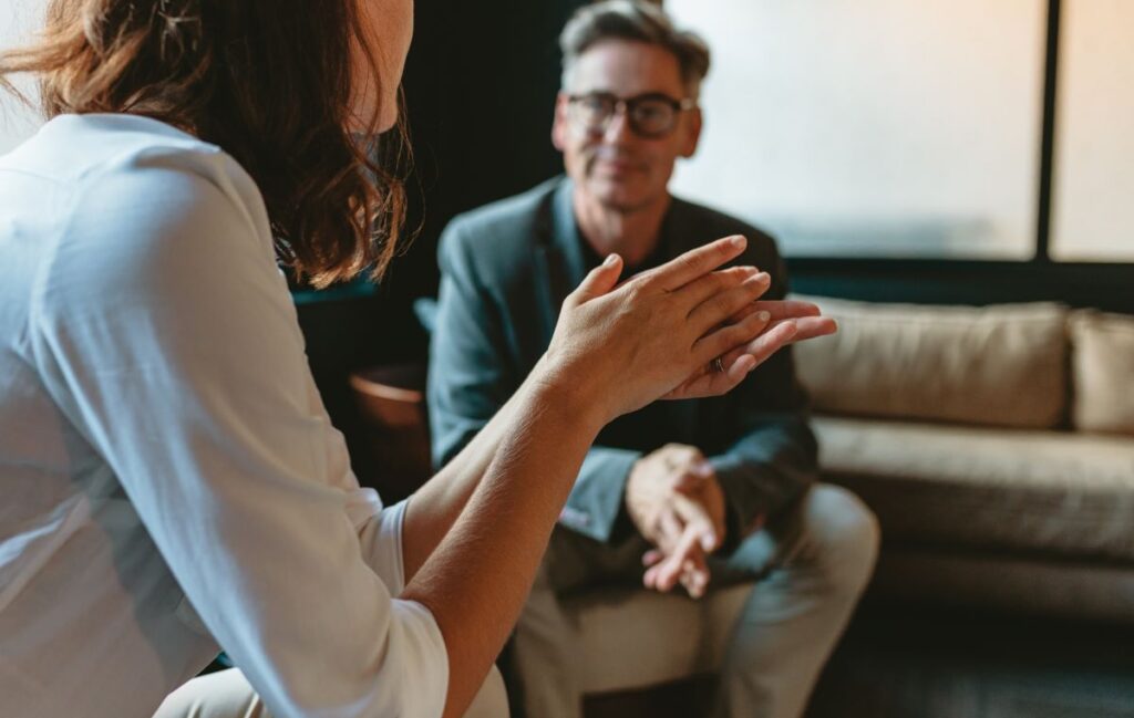 Two coworkers sit and talk with each other in an office.
