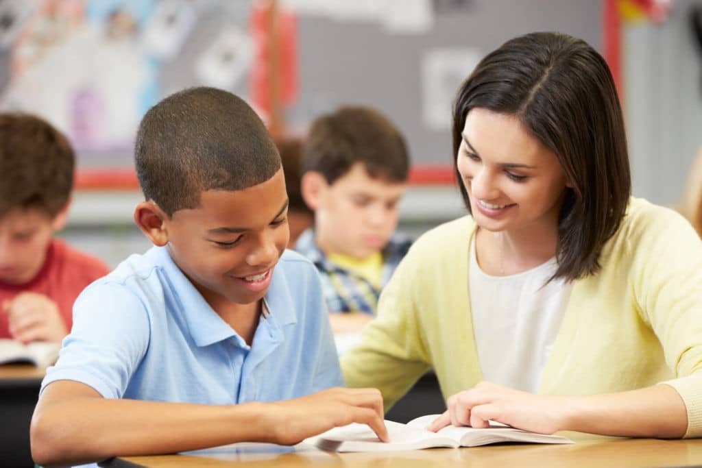 Teacher helping a young student read at his desk.